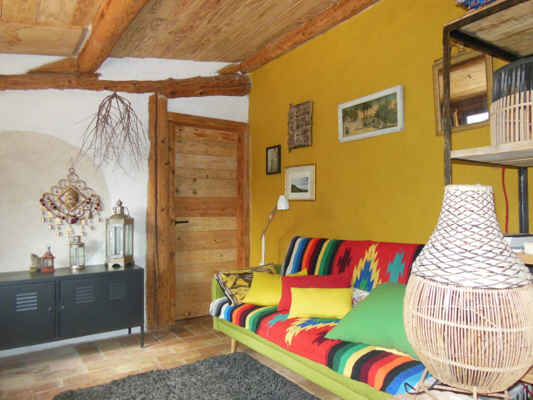 Salon intérieur chaleureux avec un canapé coloré, murs en bois et décoration rustique à Côté Corbières.