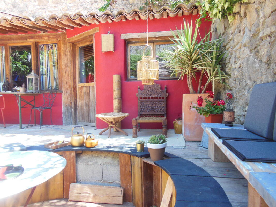 Maison dans un jardin avec une façade rouge traditionnelle, mobilier rustique et plantes décoratives à Côté Corbières.