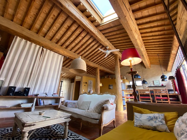 Salon spacieux avec plafond en poutres apparentes, mobilier ancien et grande luminosité naturelle à Côté Corbières.