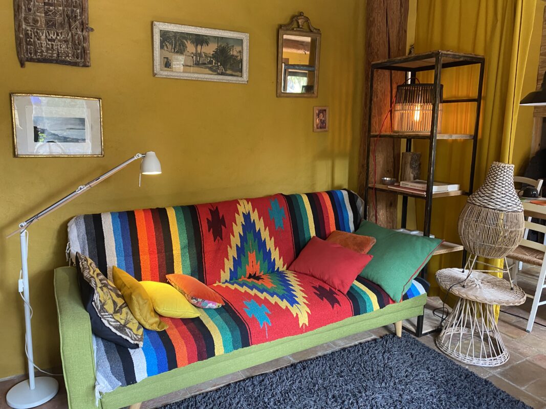 Salon coloré avec canapé recouvert d'une couverture multicolore, décoration rustique et lampe moderne dans la maison d'hôtes 'Maison dans un Jardin' à Villesèque-des-Corbières.