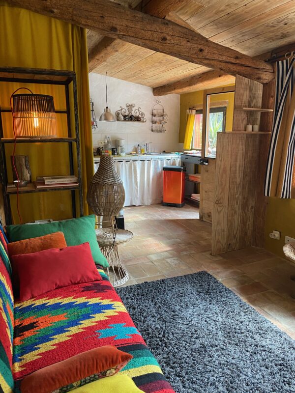 Intérieur de la maison d'hôtes 'Maison dans un Jardin' à Villesèque-des-Corbières, montrant le salon avec un canapé coloré et une cuisine ouverte.