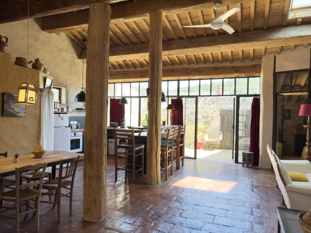 Intérieur spacieux et lumineux du loft écologique à Villesèque-des-Corbières, avec poutres apparentes en bois, cuisine ouverte et grande table à manger.