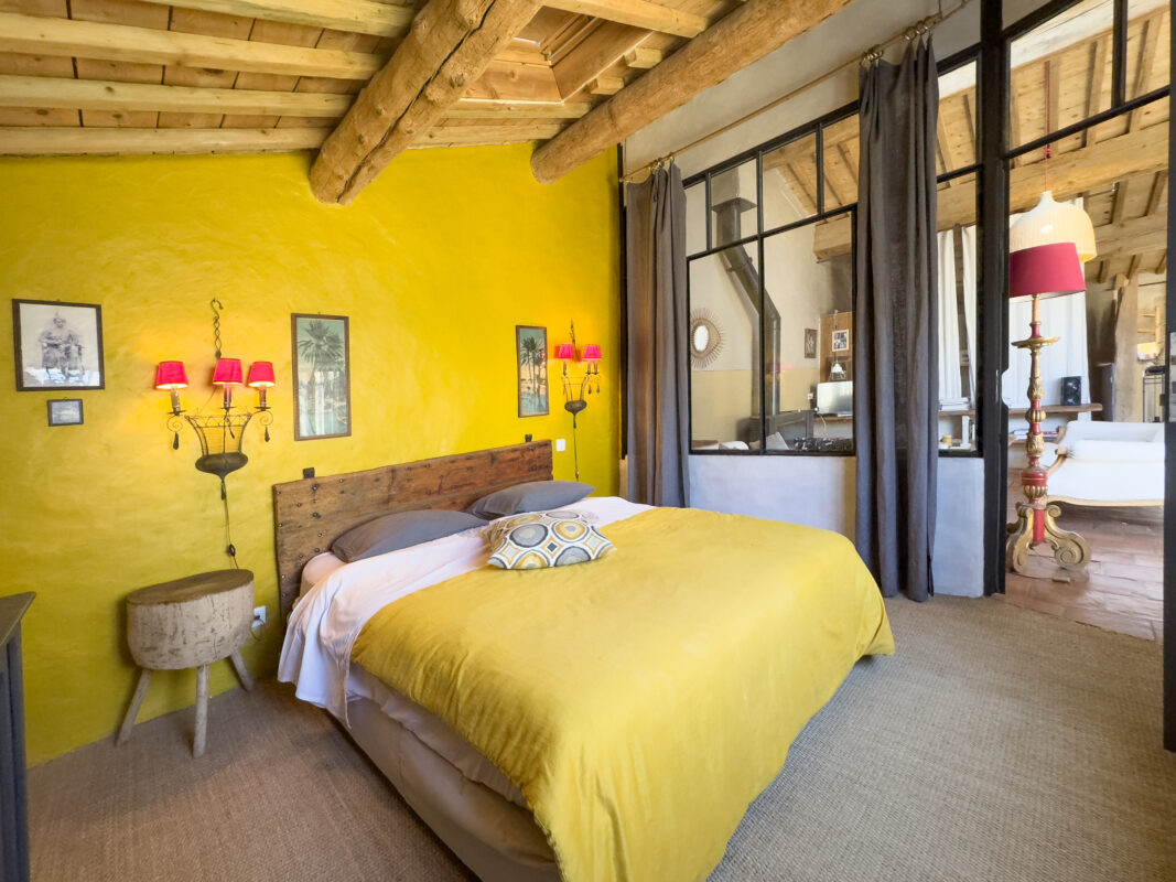 Chambre à coucher lumineuse avec des murs jaunes, poutres apparentes et décoration élégante à Côté Corbières.