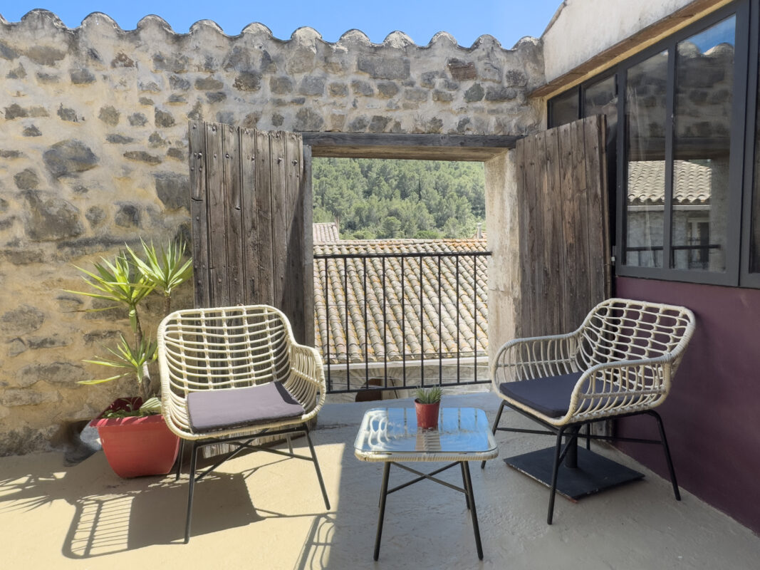 Petite terrasse ensoleillée avec vue sur les montagnes des Corbières, meublé de chaises en rotin et d'une petite table, dans le loft écologique à Villesèque-des-Corbières.