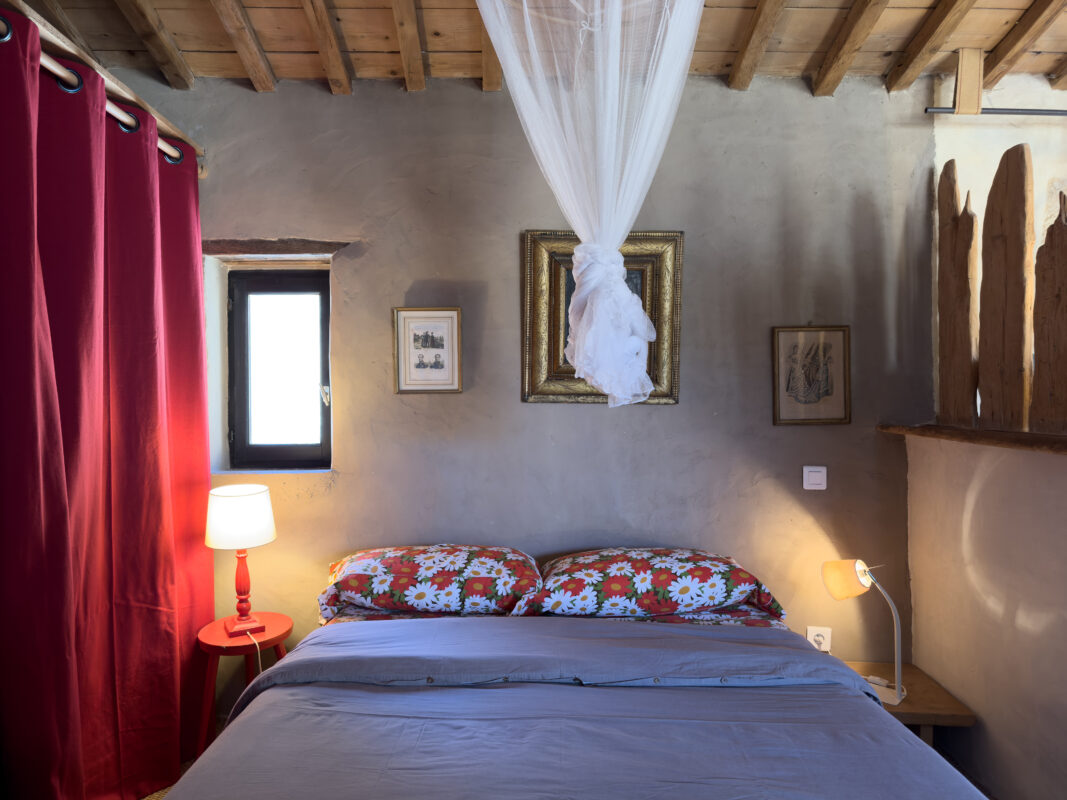 Chambre confortable et rustique dans le loft écologique de Villesèque-des-Corbières, avec lit double, voilages blancs et murs en pierre apparente.